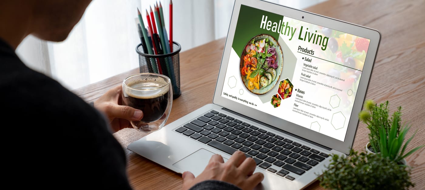 Homme buvant du café et consultant un site web de restaurant avec des salades sur un ordinateur portable