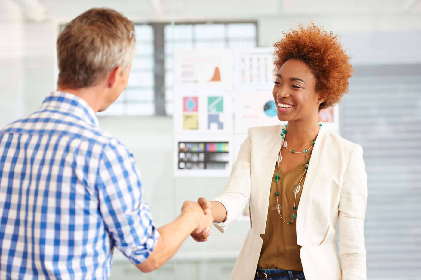 Une femme souriante et un homme se serrent la main dans un bureau avec des graphiques
